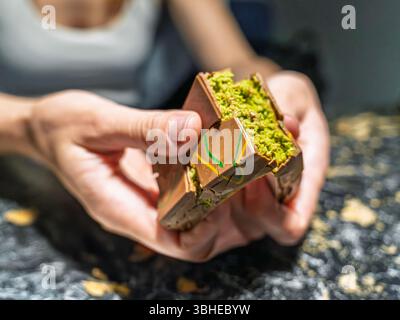 Eine detaillierte Nahaufnahme einer Frau, die die virale Dubai-Schokolade mit ihrer berühmten knusprigen Pistazienfüllung aufbricht Stockfoto