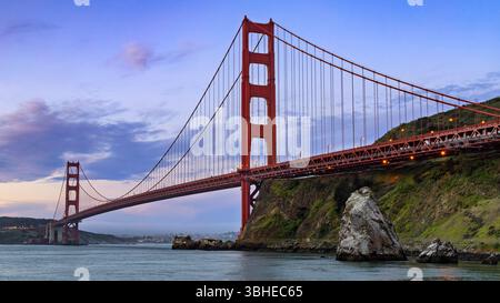 Die majestätische Golden Gate Hängebrücke erstreckt sich über ein ruhiges Gewässer und verbindet üppig grüne Hügel. Der Himmel ist mit weichen Pastelltönen A getönt Stockfoto