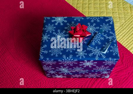 Blick von oben auf ein eingewickeltes Weihnachtsgeschenk, das auf rot-gelb gesteppten Bettüberwürfen sitzt. Stockfoto
