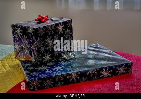 Vorderansicht von zwei Weihnachtsgeschenken, die auf gesteppten Bettüberwürfen neben einem sonnendurchfluteten Fenster sitzen. Stockfoto