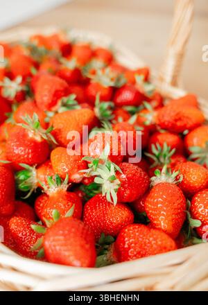 Ein Korbkorb gefüllt mit hellen, Reifen Erdbeeren auf einer Holzoberfläche. Die leuchtende rote Farbe und der frische Look der Erdbeeren heben hervor Stockfoto