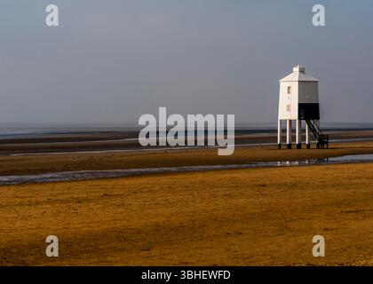 Ein weiß-schwarzer Leuchtturm steht auf Stelzen an einem Sandstrand. Die Flut ist vorbei und der nasse Sand reflektiert den Leuchtturm und den Himmel. Stockfoto