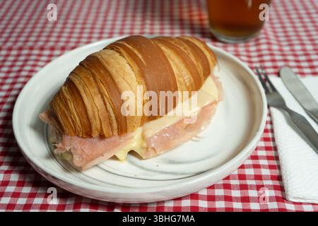 Frisch gebackenes Croissant-Sandwich mit Premium-Schinken und geschmolzenem Käse, das die goldene Kruste unterstreicht. Ausgezeichnet für Websites für Bäckerei oder Rezeptbeiträge. Stockfoto