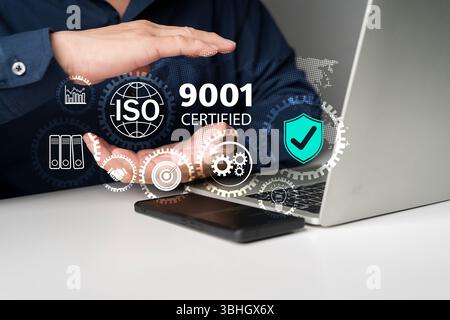 Hand mit ISO 9001-zertifiziertem Konzept mit digitalen Schnittstellensymbolen auf dem Laptop, die das Qualitätsmanagementsystem, die Geschäftsstandards und die Prozesskooperation darstellen Stockfoto