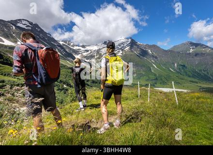 Drei Wanderer genießen die Sommerwanderung durch üppige grüne Hügel und majestätische Berge der österreichischen Alpen. Der klare blaue Himmel trägt zur atemberaubenden Landschaft aro bei Stockfoto