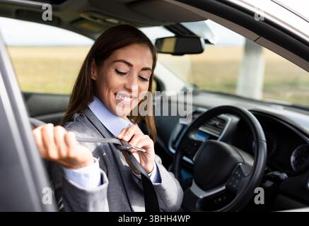 Frau lächelt, während sie im Auto sitzt. Das Innere ist modern und tagsüber gut beleuchtet Stockfoto