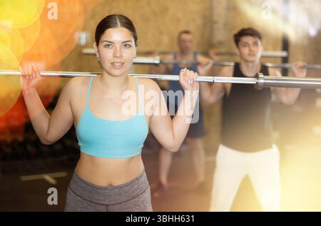 Energiegeladene junge Sportlerin, die Sit-ups mit Stange in der Nähe des Fitnessstudios anderer Leute übt Stockfoto