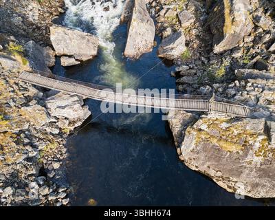 Drohnenansicht einer hölzernen Hängebrücke über einen rauschenden Fluss in einem felsigen Canyon, Norwegen. Reise, Abenteuer und wilde Natur Konzept. Stockfoto