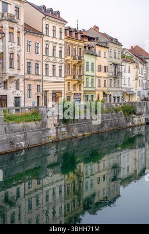Farbenfrohe historische Häuser entlang des Flusses Ljubljanica in Ljubljana, Slowenien. Die bezaubernden Fassaden spiegeln sich wunderbar auf das ruhige Flusswasser. Stockfoto