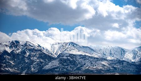 Das Bild zeigt eine majestätische, schneebedeckte Bergkette unter einem dramatischen Himmel voller großer, flauschiger Wolken. Die Berge haben eine zerklüftete und steile Stockfoto