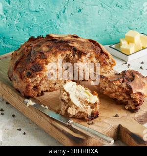 Dinkel Rosinenbrot mit Butter an der Seite – eine rustikale Frühstücks- oder Nachmittagsszene, serviert auf einem weißen Teller, Schneidebrett oder Kühlregal. Stockfoto