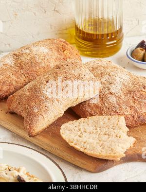 Dinkel-Ciabatta auf Holzoberfläche mit Oliven und Olivenöl im Hintergrund – ein rustikales Brot im mediterranen Stil, perfekt für Aperitif. Stockfoto