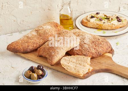 Dinkel-Ciabatta auf Holzoberfläche mit Oliven und Olivenöl im Hintergrund – ein rustikales Brot im mediterranen Stil, perfekt für Aperitif. Stockfoto