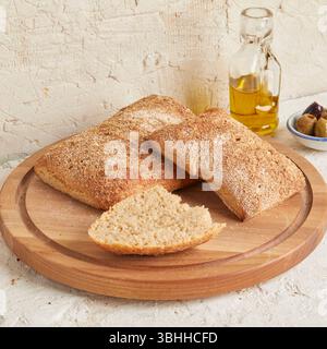 Dinkel-Ciabatta auf Holzoberfläche mit Oliven und Olivenöl im Hintergrund – ein rustikales Brot im mediterranen Stil, perfekt für Aperitif. Stockfoto