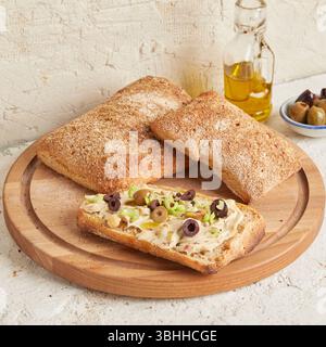 Dinkel-Ciabatta auf Holzoberfläche mit Oliven und Olivenöl im Hintergrund – ein rustikales Brot im mediterranen Stil, perfekt für Aperitif. Stockfoto