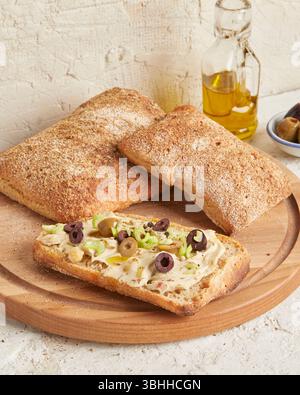 Dinkel-Ciabatta auf Holzoberfläche mit Oliven und Olivenöl im Hintergrund – ein rustikales Brot im mediterranen Stil, perfekt für Aperitif. Stockfoto