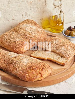 Dinkel-Ciabatta auf Holzoberfläche mit Oliven und Olivenöl im Hintergrund – ein rustikales Brot im mediterranen Stil, perfekt für Aperitif. Stockfoto