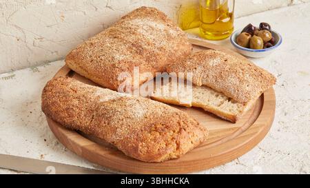 Dinkel-Ciabatta auf Holzoberfläche mit Oliven und Olivenöl im Hintergrund – ein rustikales Brot im mediterranen Stil, perfekt für Aperitif. Stockfoto