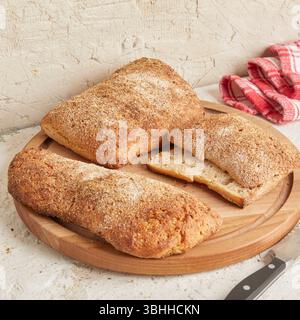Dinkel-Ciabatta auf Holzoberfläche mit Oliven und Olivenöl im Hintergrund – ein rustikales Brot im mediterranen Stil, perfekt für Aperitif. Stockfoto