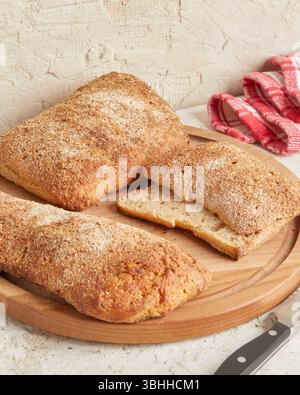 Dinkel-Ciabatta auf Holzoberfläche mit Oliven und Olivenöl im Hintergrund – ein rustikales Brot im mediterranen Stil, perfekt für Aperitif. Stockfoto