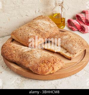 Dinkel-Ciabatta auf Holzoberfläche mit Oliven und Olivenöl im Hintergrund – ein rustikales Brot im mediterranen Stil, perfekt für Aperitif. Stockfoto