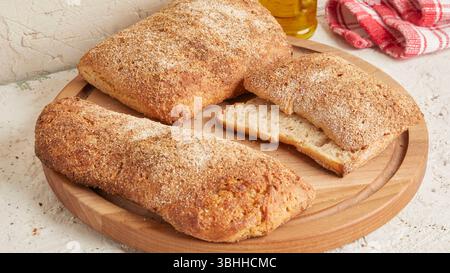 Dinkel-Ciabatta auf Holzoberfläche mit Oliven und Olivenöl im Hintergrund – ein rustikales Brot im mediterranen Stil, perfekt für Aperitif. Stockfoto