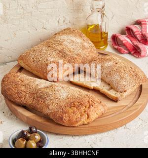 Dinkel-Ciabatta auf Holzoberfläche mit Oliven und Olivenöl im Hintergrund – ein rustikales Brot im mediterranen Stil, perfekt für Aperitif. Stockfoto