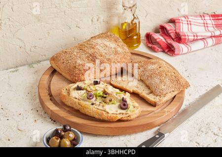 Dinkel-Ciabatta auf Holzoberfläche mit Oliven und Olivenöl im Hintergrund – ein rustikales Brot im mediterranen Stil, perfekt für Aperitif. Stockfoto