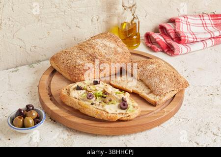 Dinkel-Ciabatta auf Holzoberfläche mit Oliven und Olivenöl im Hintergrund – ein rustikales Brot im mediterranen Stil, perfekt für Aperitif. Stockfoto