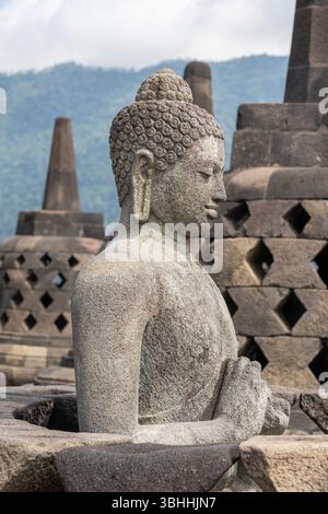 Nahaufnahme der antiken Vairocana buddha Statue in situ mit Stupas im Hintergrund im historischen Borobudur, Magelang, Zentral-Java, Indonesien Stockfoto