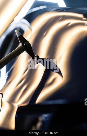 Bei der lacklosen Dellen-Reparatur bei PDR werden Dellen unter Lichtreflexion für Präzision geschlagen. Der Techniker verwendet PDR-Werkzeuge, um Dellen von der Motorhaube zu entfernen Stockfoto