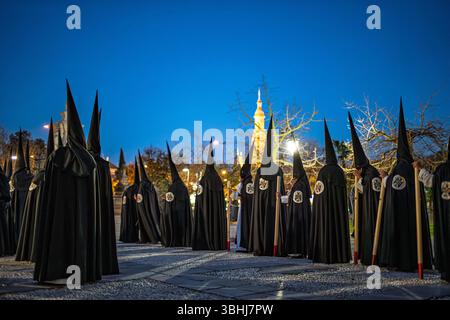 Nazarener aus der Hermandad de Santa Genoveva treffen sich zu einer feierlichen Prozession in Sevilla, Andalusien, um die Karwoche in der Abenddämmerung zu feiern. Stockfoto