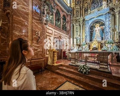 In Sevilla blickt eine junge Frau aufmerksam, während sie vor der verehrten Esperanza Macarena betet, umgeben von verzierten Dekorationen. Stockfoto