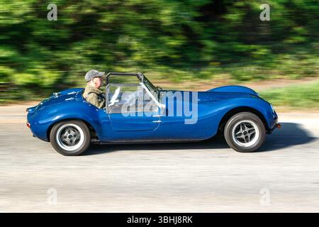 Seitenansicht eines klassischen blauen Sportwagens mit Autotuning gemini, der von einem Mann auf einer Straße mit einem verschwommenen grünen Hintergrund gefahren wird, was auf Geschwindigkeit hindeutet Stockfoto