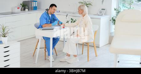 Männlicher Endokrinologe mit Lanzettenstift zur Messung des Blutzuckerspiegels weiblicher Patientinnen in der Klinik Stockfoto