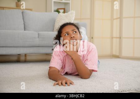 Nachdenkliches afroamerikanisches Mädchen, das zu Hause auf dem Boden liegt Stockfoto