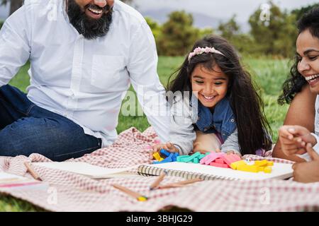 Glückliche indische Familie, die Spaß beim Spielen mit ihrer Tochter im Freien im Stadtpark hat - Sommerzeit und Elternschaftskonzept - Fokus auf Kindergesicht Stockfoto