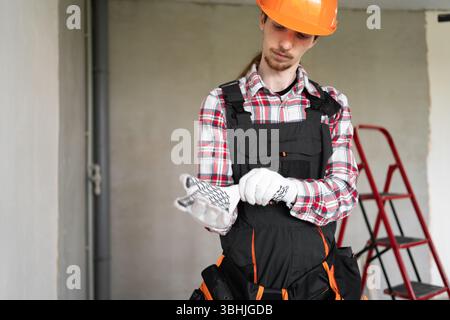Bauarbeiter oder junger Bauarbeiter, der vor der Arbeit Handschuhe trägt und im Haus zur Renovierung steht Stockfoto