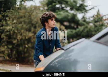 Junger Mann, der sein Auto an einem regnerischen Tag im Freien überprüft Stockfoto