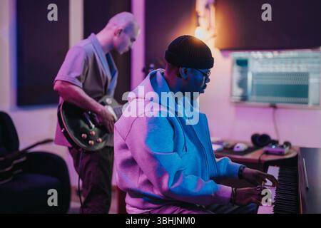 Musiker arbeiten in einem modernen Tonstudio zusammen. Einer spielt das Keyboard, der andere spielt eine Gitarre. Stockfoto