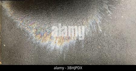 Farbenfrohe Regenbogenmuster entstanden durch Öl auf einer strukturierten, nassen Straßenoberfläche. Das abstrakte Erscheinungsbild zeigt eine Mischung aus lebendigem h Stockfoto