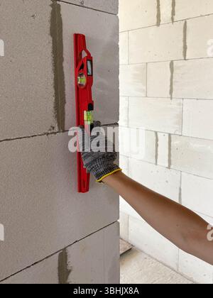 Ein Erbauer wendet eine Blasenebene auf eine neue Wand auf einer Baustelle an, um deren Ebenheit zu prüfen. Messgeräte auf der Baustelle. Stockfoto