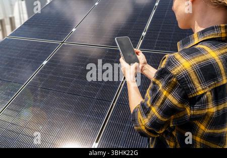 Weibliche Wartungstechnikerin überprüft die Leistung des Solarmoduls auf dem Smartphone Stockfoto