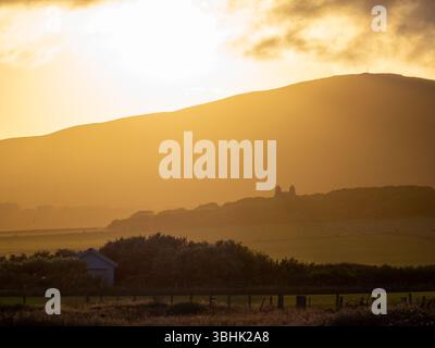 Die Sonne untergeht hinter den Hügeln von Orphir, Festland, Orkney, Schottland, mit warmen Lichtstrahlen, die die Felder erleuchten Stockfoto