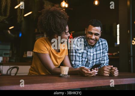 Fröhliches junges Paar mit Smartphone und Kaffee im modernen Café Stockfoto