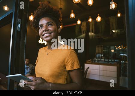 Lächelnde junge Besitzerin, die ein digitales Tablet in der Nähe des Cafés hält Stockfoto
