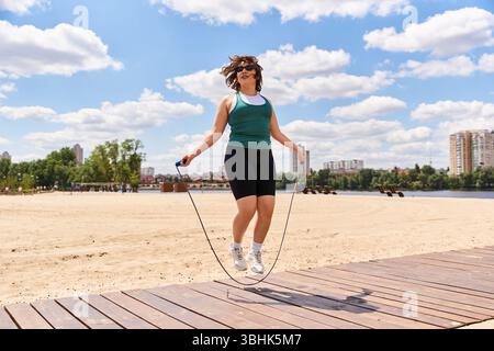 Junge Frau springt Seil auf Sand, lebhafte Skyline hinter ihr, genießt Fitness. Stockfoto