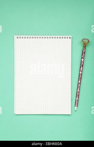 Ein Notizbuch mit einer leeren Seite und einem Stift auf mintfarbenem Hintergrund. Vertikales Foto Stockfoto