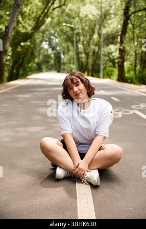 Eine junge Frau sitzt auf der Straße, sonnt sich im hellen Sonnenlicht und ist von üppigem Grün umgeben. Stockfoto
