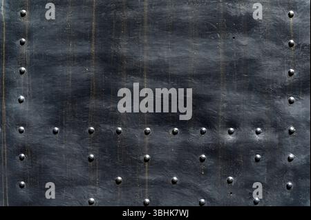 Nieten verzieren einen grunge-schwarzen Metallhintergrund und schaffen eine industrielle abstrakte Textur Stockfoto